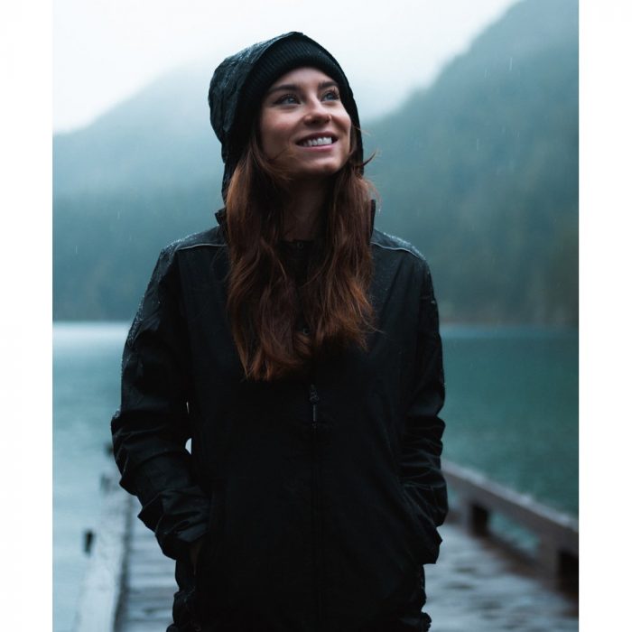 A woman wearing a hooded waterproof jacket next to a lake on a rainy day.